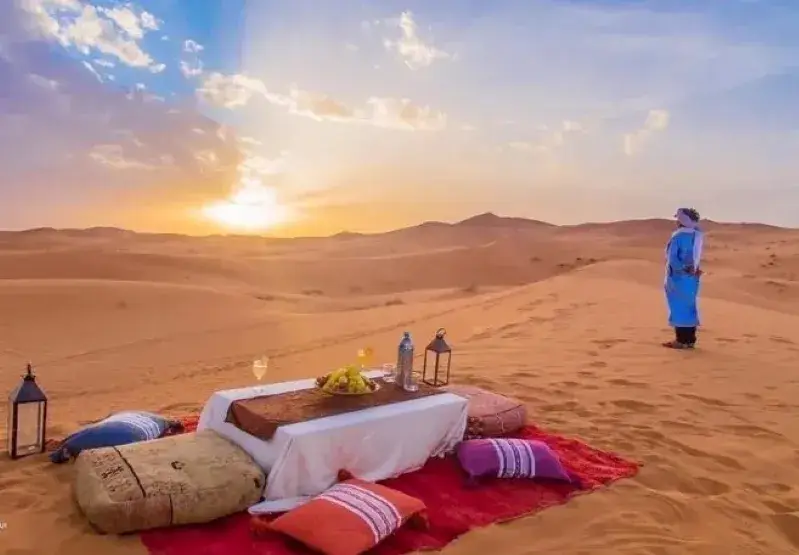 A romantic dinner set against a vibrant Sahara Desert sunset, showcasing the beauty of Marrakech tours.