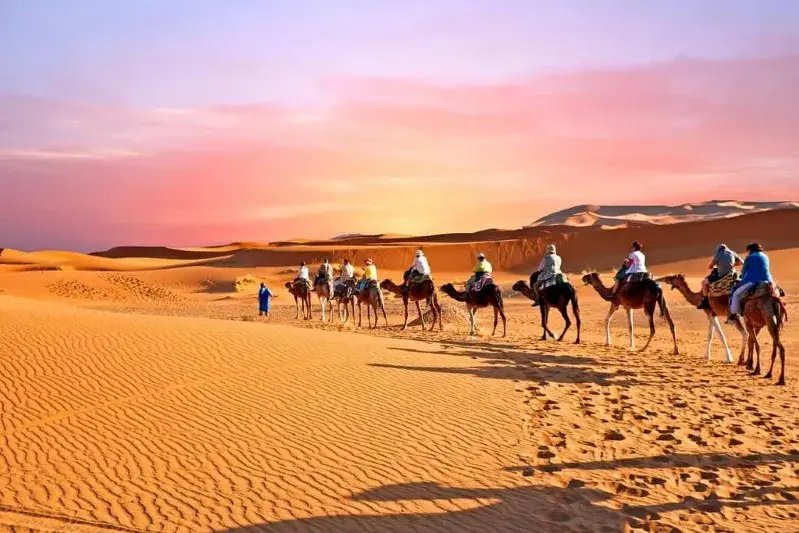 A group of tourists riding camels through the sandy desert landscape during a Marrakech tour.