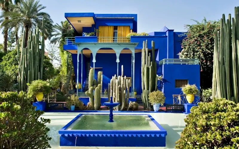 A blue house surrounded by cactus plants and a fountain, showcasing a charming Marrakech attraction.